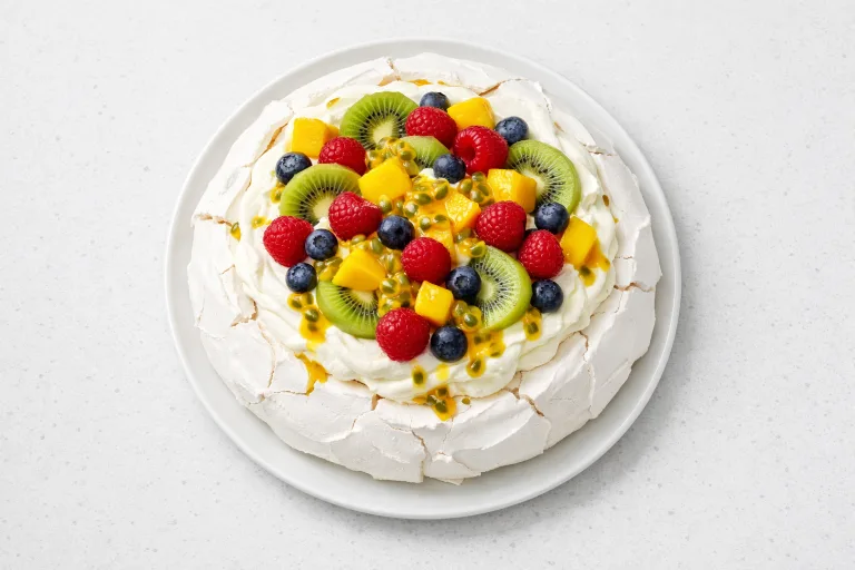 Australian Christmas pavlova topped with whipped cream, tropical fruit, and berries on a white ceramic plate