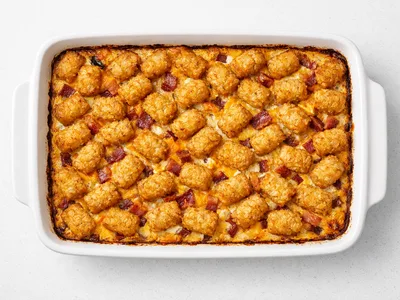 Bacon and egg tater tot casserole in a white baking dish, golden crispy tots on top with melted cheese and bacon