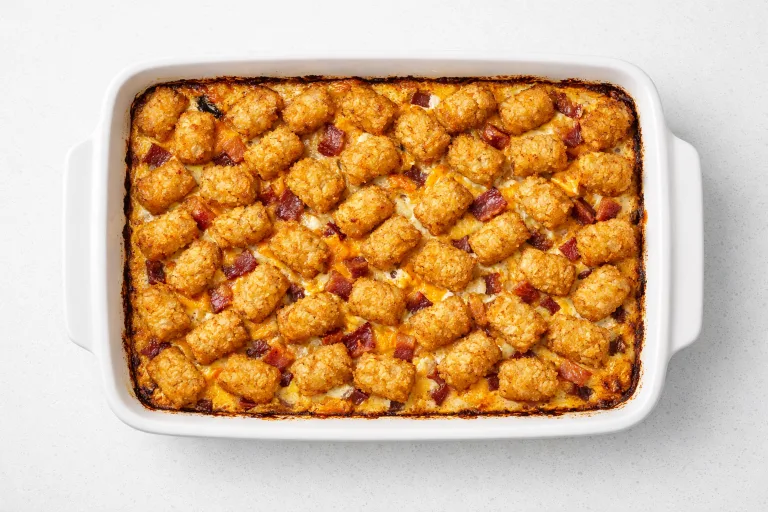 Bacon and egg tater tot casserole in a white baking dish, golden crispy tots on top with melted cheese and bacon