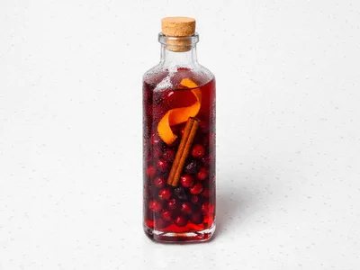 Bottle of deep red Christmas infused vodka with cranberries, cinnamon stick, and orange peel visible through the glass
