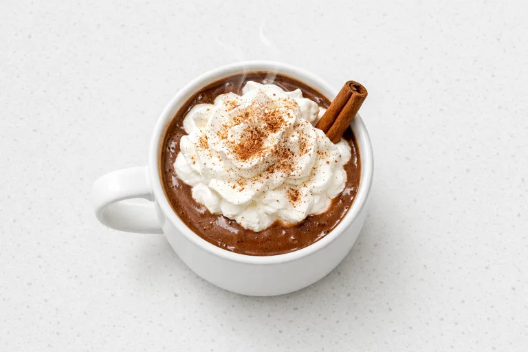 Bourbon gingerbread hot chocolate in a white mug topped with whipped cream and a cinnamon stick