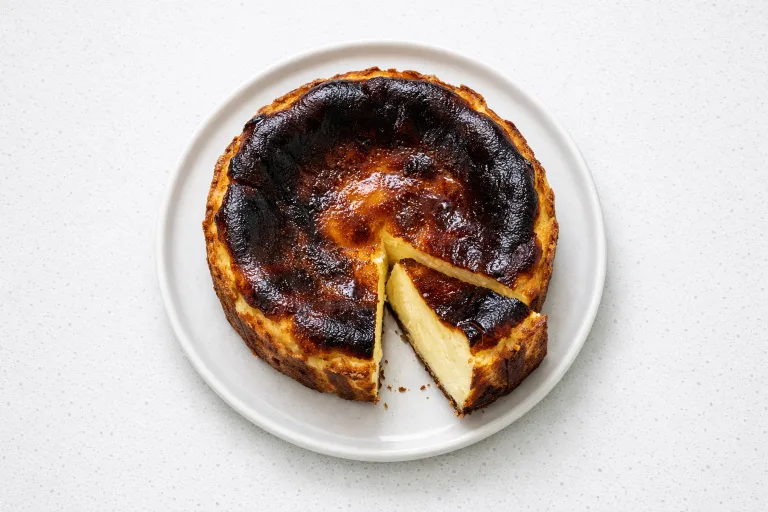 Burnt Basque cheesecake with deeply caramelized top and creamy custard interior on a white plate