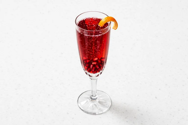 Christmas champagne cocktail with pomegranate arils and orange peel in a crystal flute