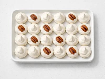 Christmas divinity candy drops on a white tray, some topped with pecan halves