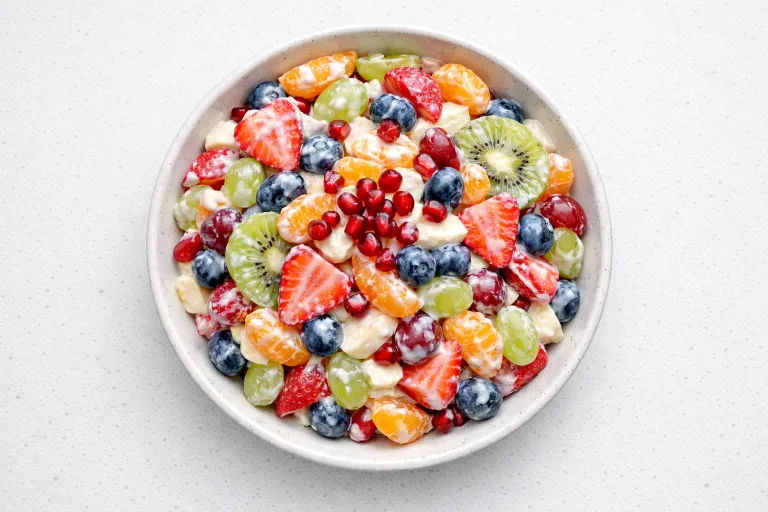 Christmas fruit salad with strawberries, kiwi, pomegranate, grapes, and whipped cream in a white bowl