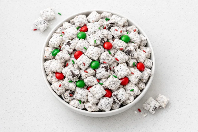Christmas puppy chow with powdered sugar coated Chex cereal, sprinkles, and holiday M&Ms in a white bowl