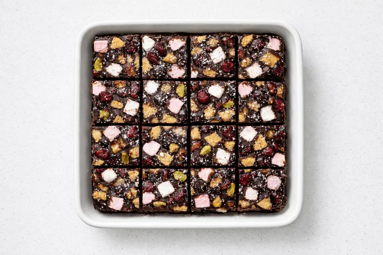 Christmas rocky road squares with marshmallows, cranberries, and pistachios in dark chocolate, cut into portions in a white baking dish