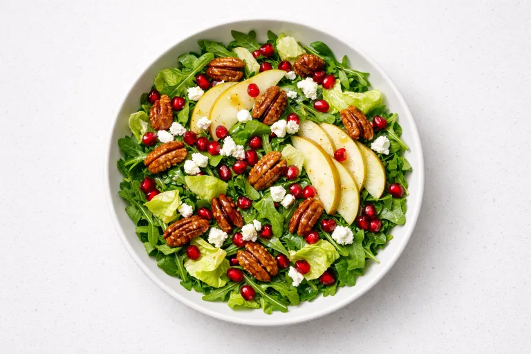 Christmas salad with pomegranate seeds, candied pecans, goat cheese, and pear slices in a white bowl