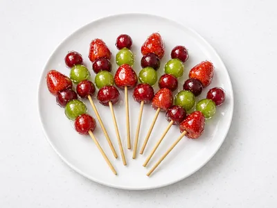 Christmas tanghulu skewers with strawberries, grapes, and cranberries coated in glassy sugar shell on a white plate