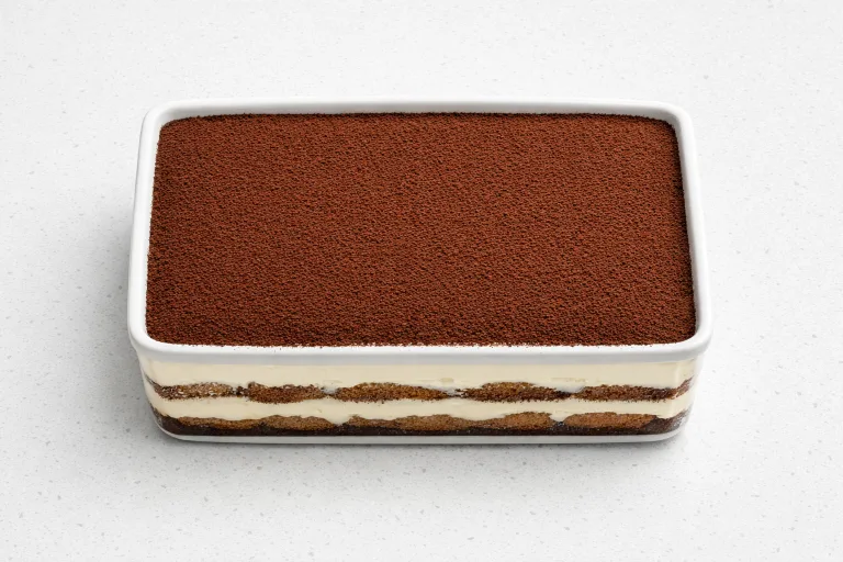 Christmas tiramisu in a white ceramic dish dusted with dark cocoa powder, showing distinct layers of mascarpone cream and espresso-soaked ladyfingers