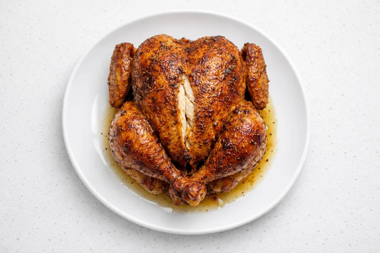 Crispy air fryer roast chicken on a white platter, golden skin with herbs, juices on the plate