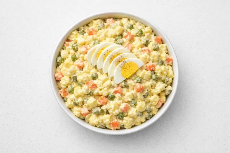 Czech potato salad bramborovy salat in a white ceramic bowl with diced vegetables and egg garnish