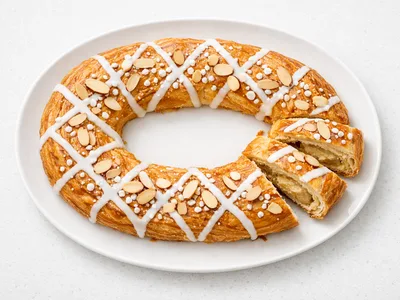 Danish kringle pastry ring with almond filling, white icing, and pearl sugar on a white plate
