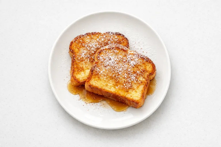 Eggnog French toast on a white plate with powdered sugar and maple syrup
