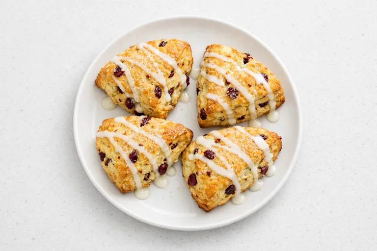 Freshly baked cranberry orange scones with orange glaze on a white ceramic plate