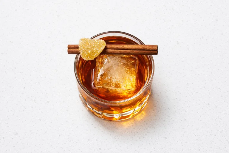 Gingerbread old fashioned cocktail in a crystal rocks glass with candied ginger and cinnamon stick garnish
