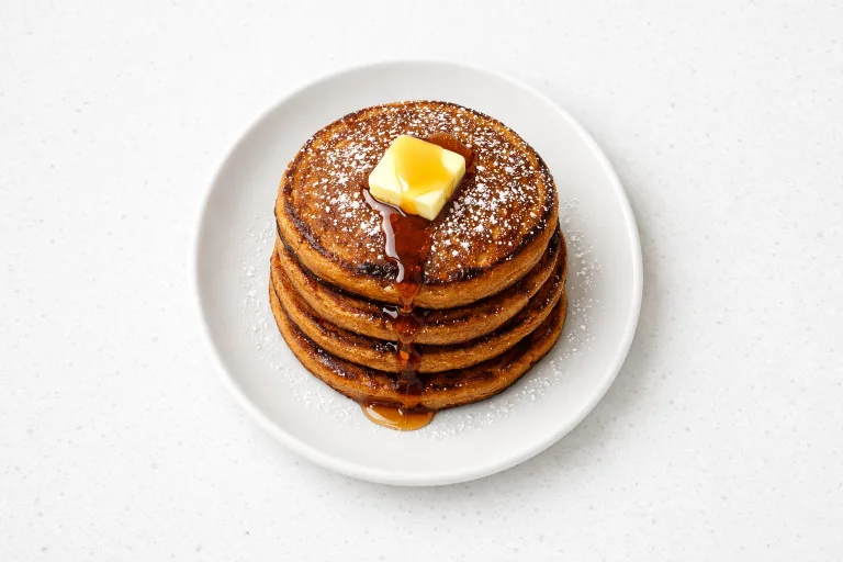 Stack of fluffy gingerbread pancakes with melting butter and maple syrup on a white plate