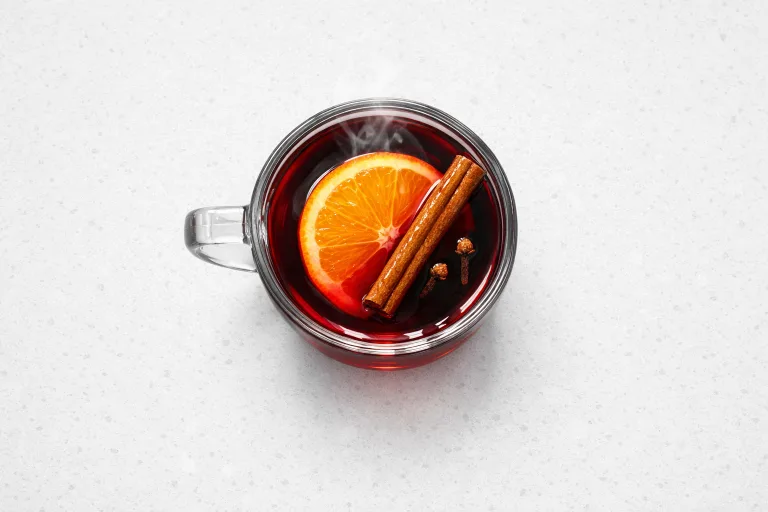 Glass mug of Czech mulled wine svarak with orange slice and cinnamon stick, steam rising