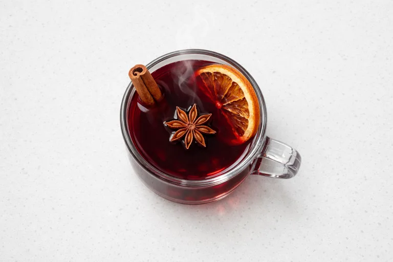 Glass mug of non-alcoholic mulled wine made with grape juice, cinnamon stick, orange slice, and star anise
