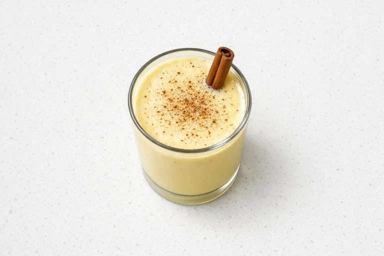 Glass of classic homemade eggnog topped with freshly grated nutmeg and a cinnamon stick