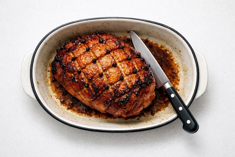 Glazed Christmas gammon joint with caramelised honey mustard glaze and clove-studded diamond scoring, freshly carved in a roasting dish