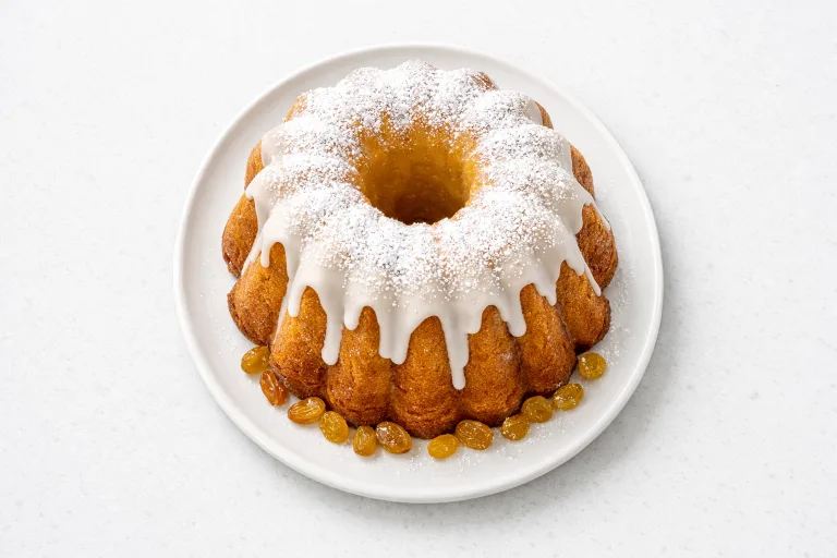 Glazed Polish babka bread on a white plate, tall fluted bundt shape with white drizzled icing