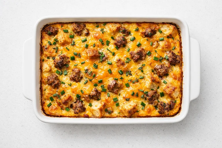 Golden-brown Christmas breakfast casserole with sausage, melted cheddar, and fresh herbs in a white baking dish