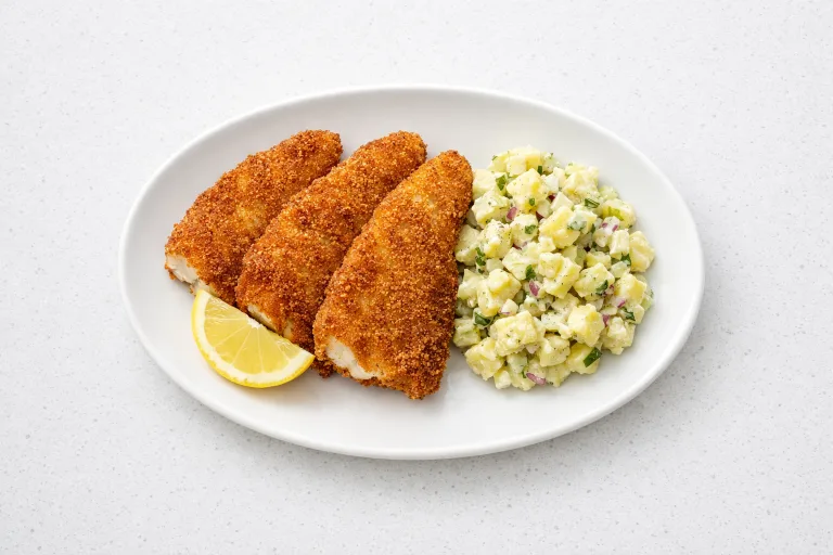 Golden fried Czech Christmas carp fillets on a white plate with lemon wedge and potato salad