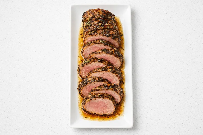 Herb-crusted Christmas pork tenderloin sliced into medallions on a white platter, showing juicy interior and garlic rosemary crust