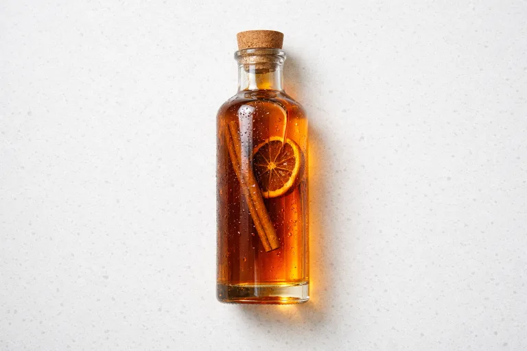 Homemade Christmas liqueur in a clear glass bottle with cinnamon stick and dried orange, amber-golden color