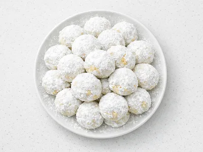 Mexican wedding cookies (polvorones) piled on a white plate, dusted with powdered sugar to resemble snowballs