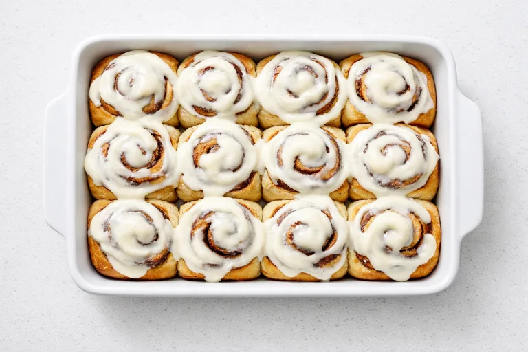 Overnight cinnamon rolls in a white baking dish with cream cheese frosting melting over golden-brown swirls