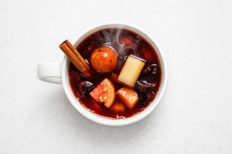 Ponche navideño in a white ceramic mug with tejocote, cinnamon stick, and steam rising