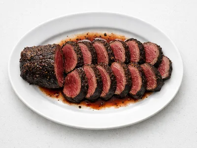 Sliced Christmas venison loin roast on a white platter, showing a red-pink interior with a dark juniper and herb crust
