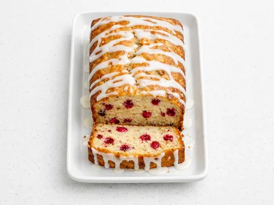 Sliced cranberry orange bread with orange glaze on a white ceramic plate, showing bright red cranberry pieces throughout the golden crumb
