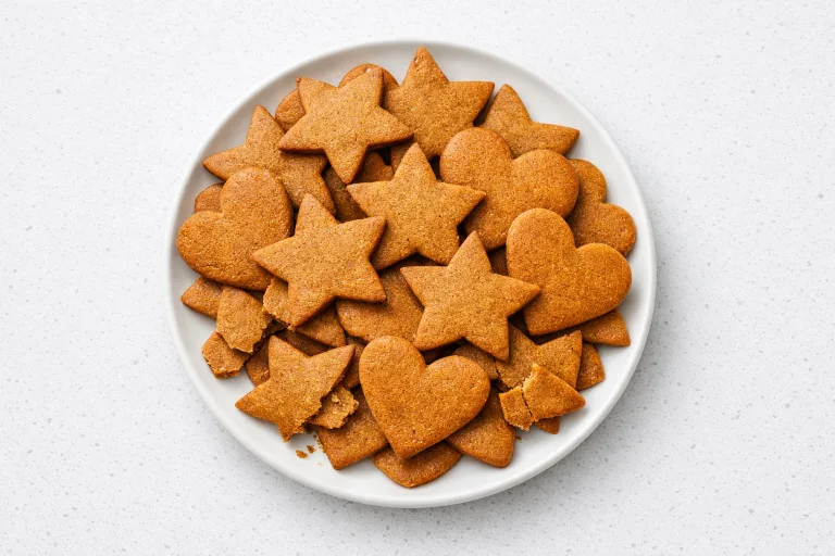 Stack of thin crisp pepparkakor Swedish ginger cookies in star and heart shapes on a white ceramic plate
