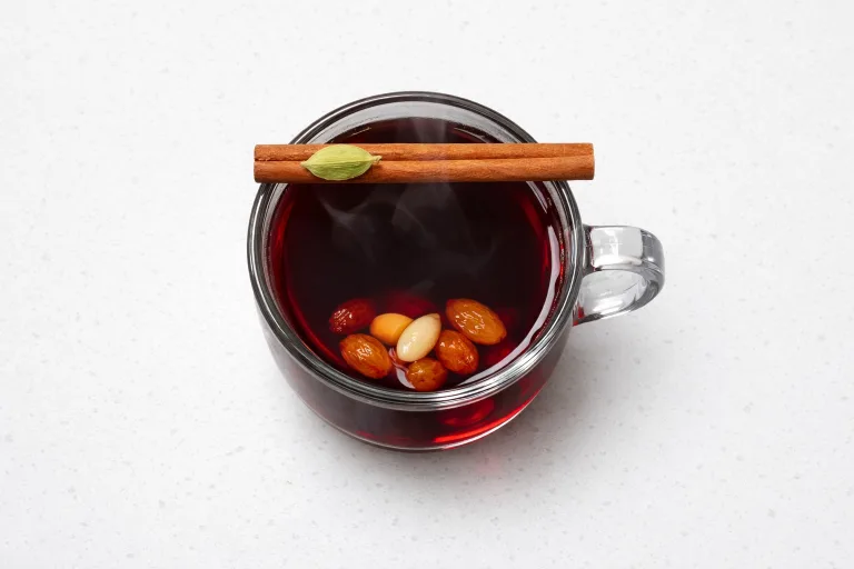 Swedish glogg in a glass mug with almonds, raisins, and a cinnamon stick