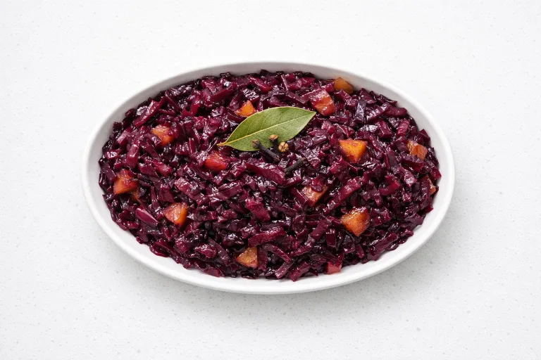 Traditional German Rotkohl braised red cabbage in a white ceramic serving dish, deep purple and glossy with apple pieces