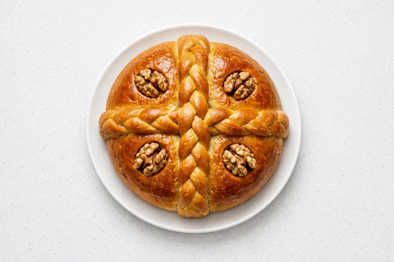 Traditional Greek christopsomo Christmas bread with dough cross and walnuts on a white plate
