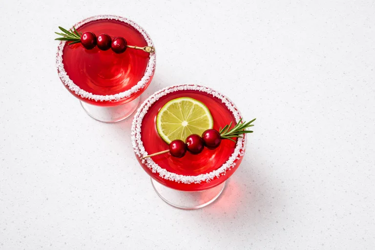Two cranberry Christmas margaritas in sugar-rimmed coupe glasses garnished with rosemary and cranberries