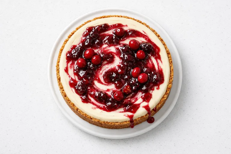 White chocolate cranberry cheesecake with glossy red cranberry topping on a white ceramic stand