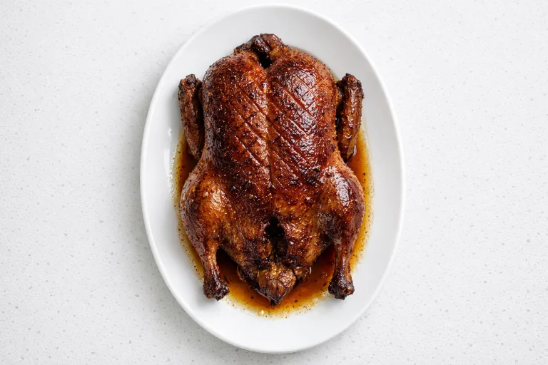 Whole Christmas roast duck with crispy golden-brown skin on a white serving platter